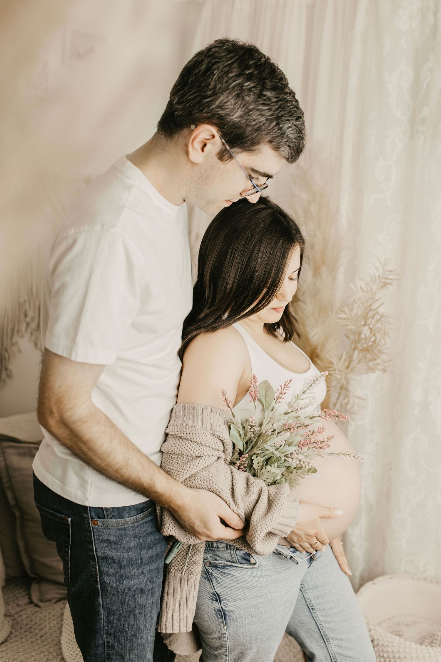 Couple embracing during intimate maternity photoshoot with dried floral decor.