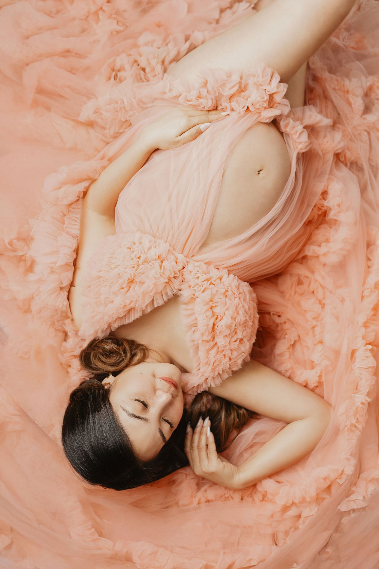 Dreamy maternity photos in soft peach tones with flowing fabric and romantic styling.
