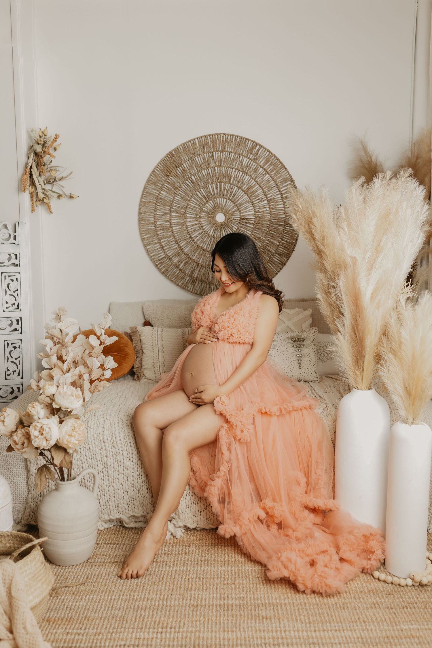 Boho maternity session with circular wall decor, pampas grass, and flowing peach dress.
