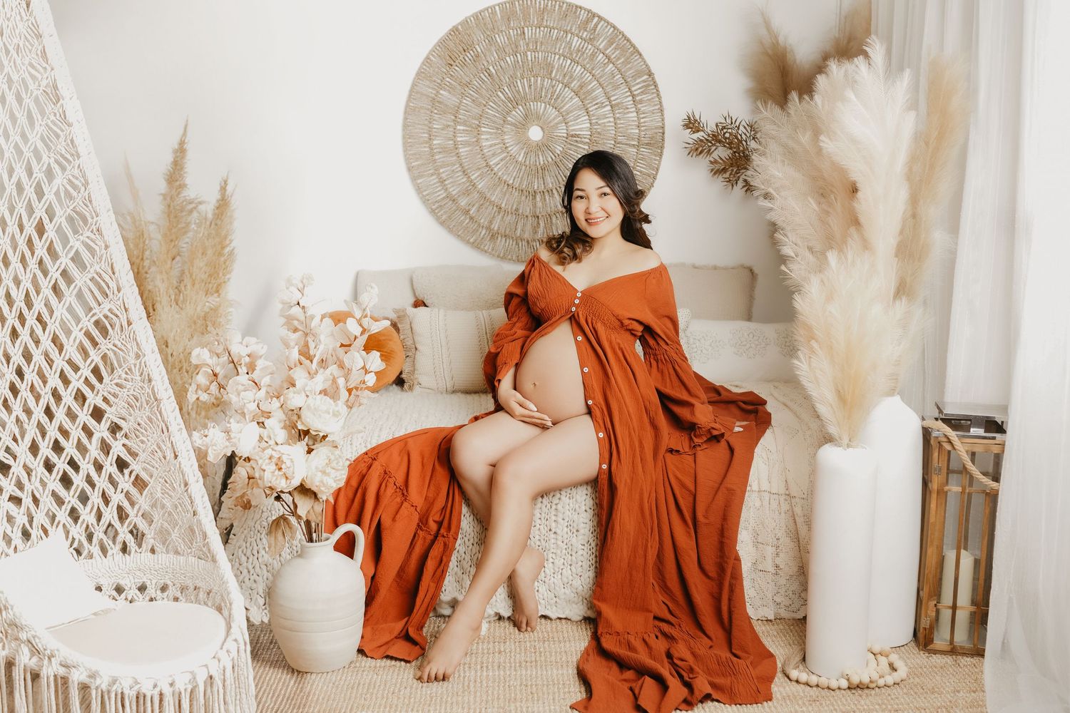 Elegant maternity photo with burnt orange dress in boho setting with pampas grass and woven decor elements.