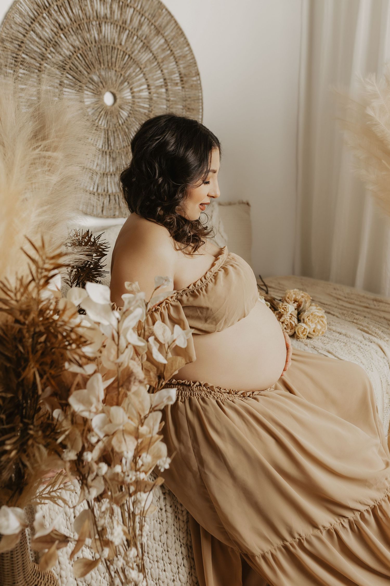 Ethereal boho photoshoot featuring a beige dress against a circular woven wall hanging and dried floral arrangements.