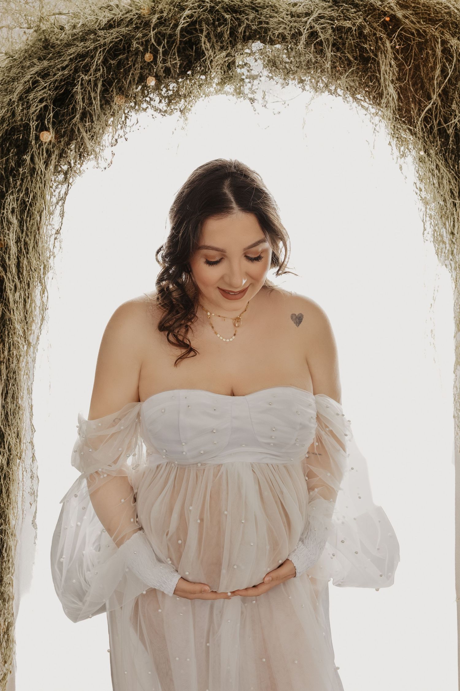 Ethereal maternity photos in white lace dress against rustic backdrop show tender moments of pregnancy.