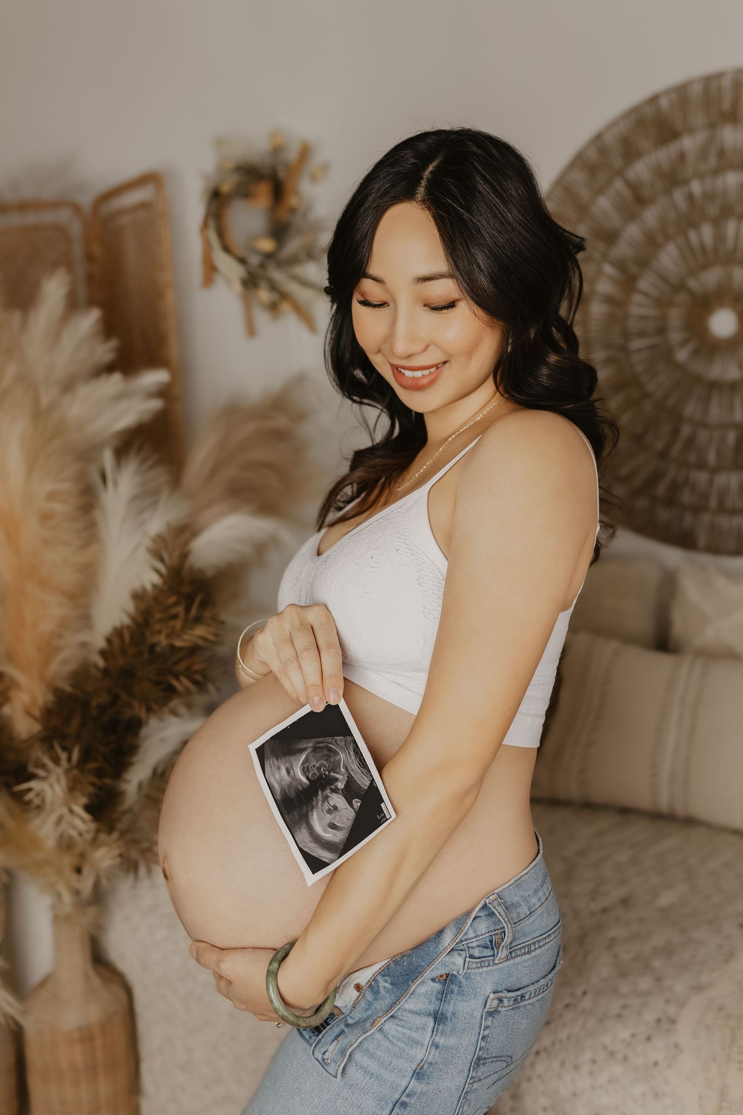 A series of intimate maternity photos showing a woman in denim and white holding an ultrasound photo in a warm-toned setting.