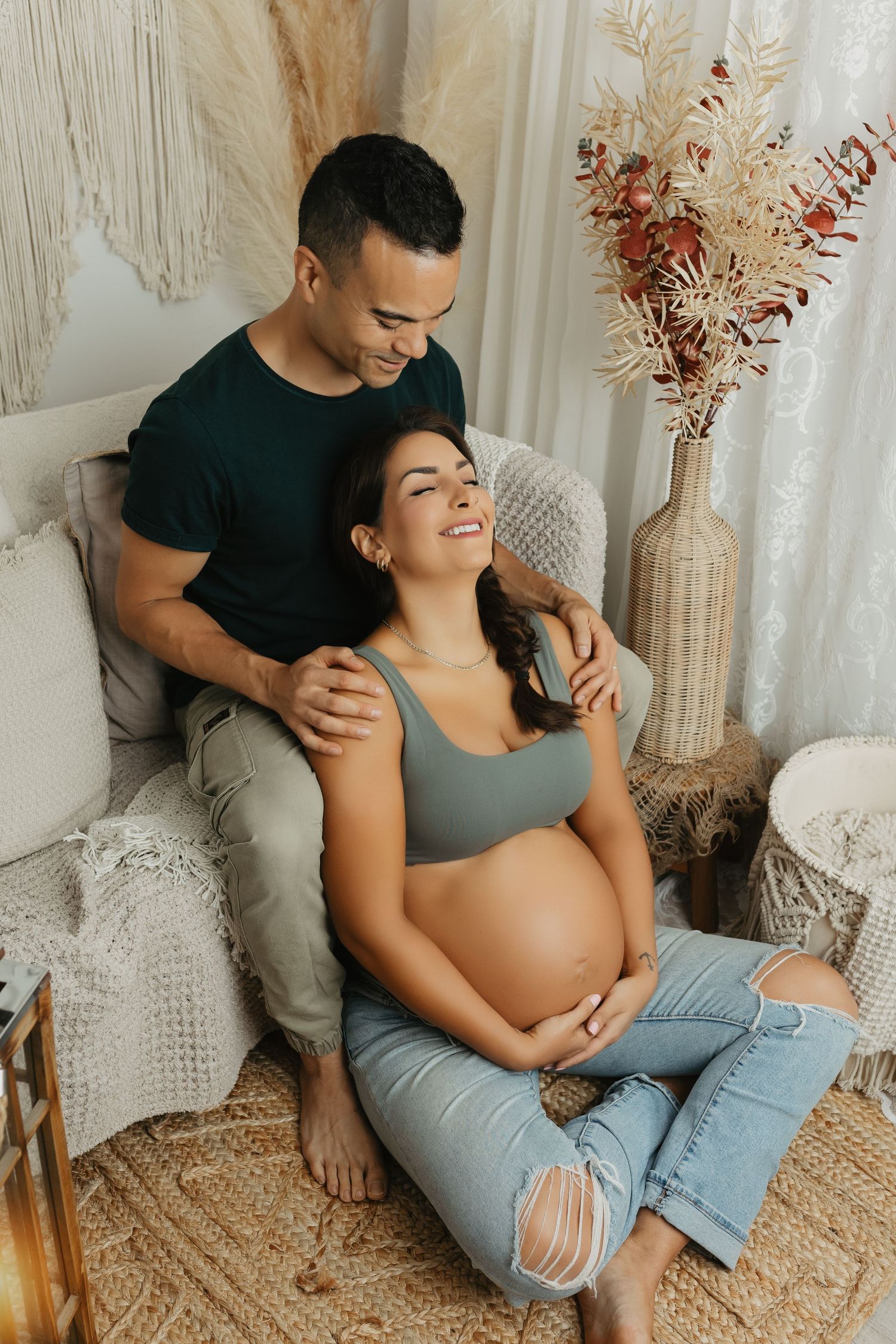 Couple lounging on woven rug during casual maternity photoshoot.