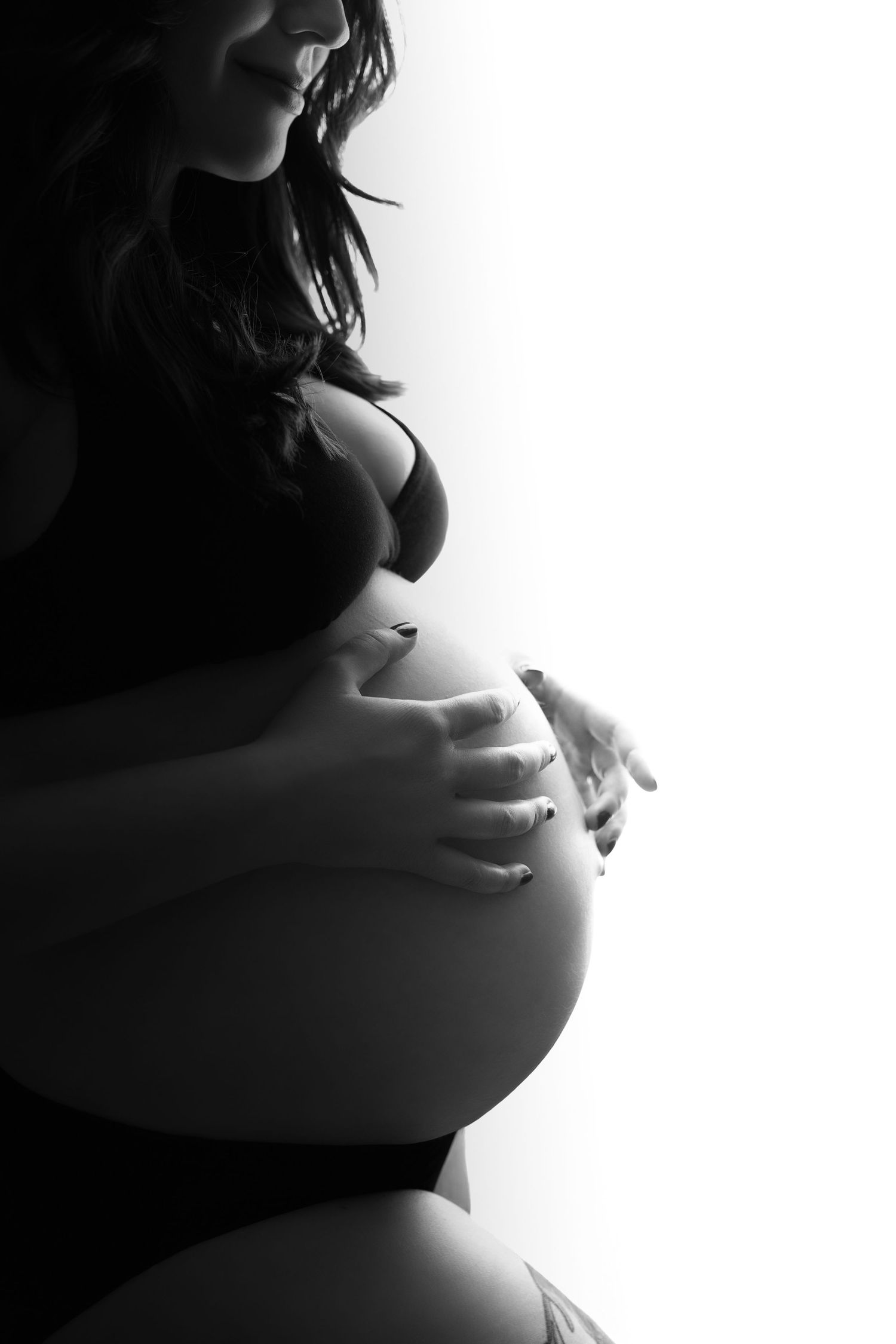 Dramatic black and white silhouette of pregnant belly with hands in artistic lighting.