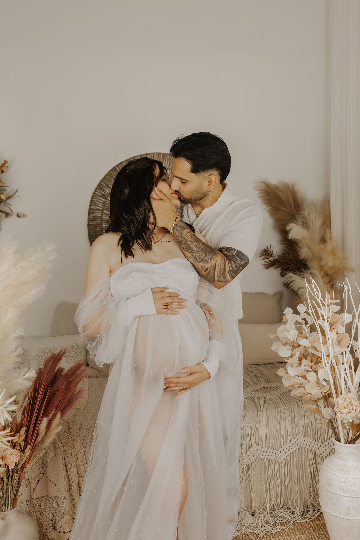 Couple sharing a tender moment during a boho maternity photoshoot with pampas grass decor in soft neutral tones.