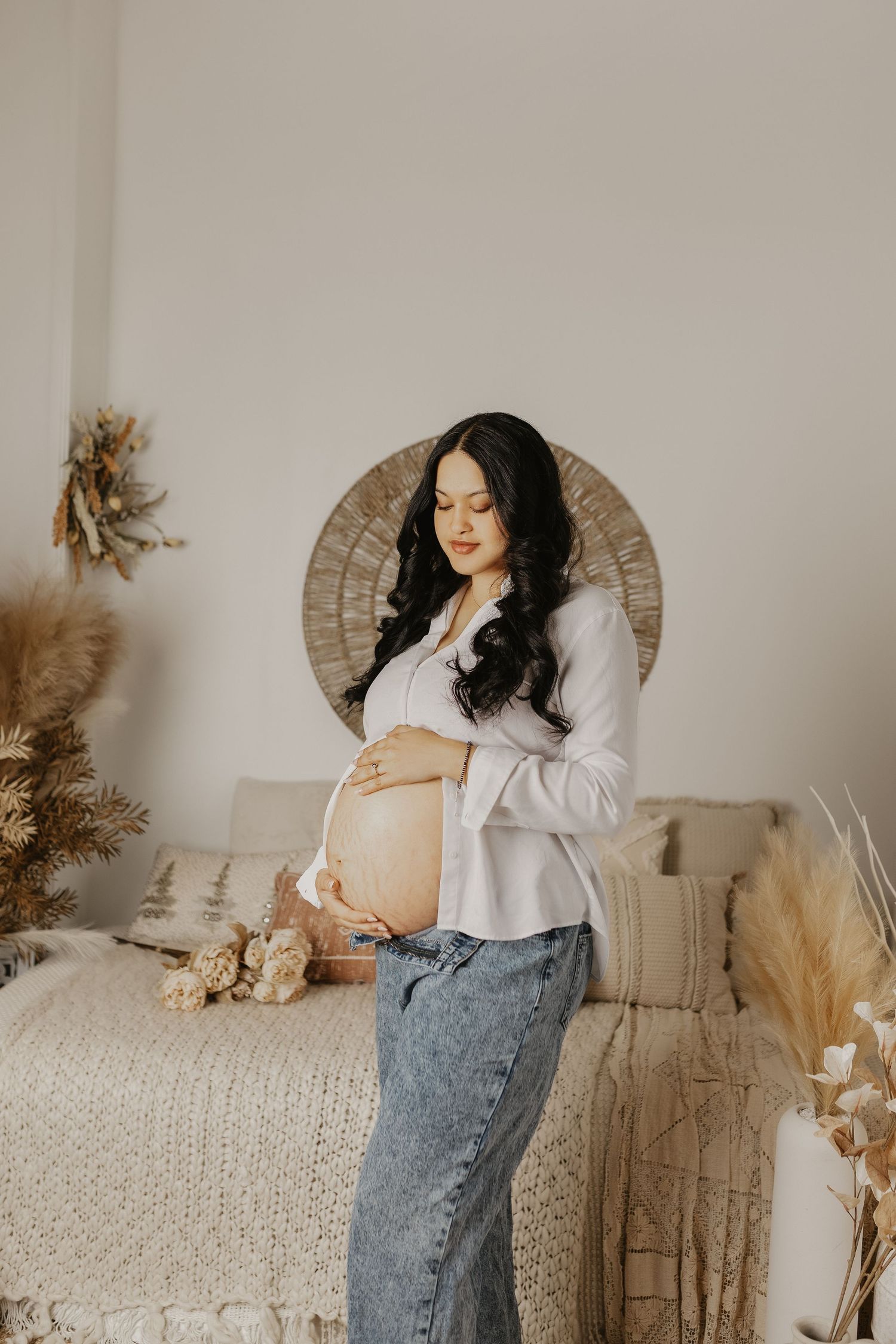 Casual maternity photos with white sweater and jeans against neutral boho backdrop.