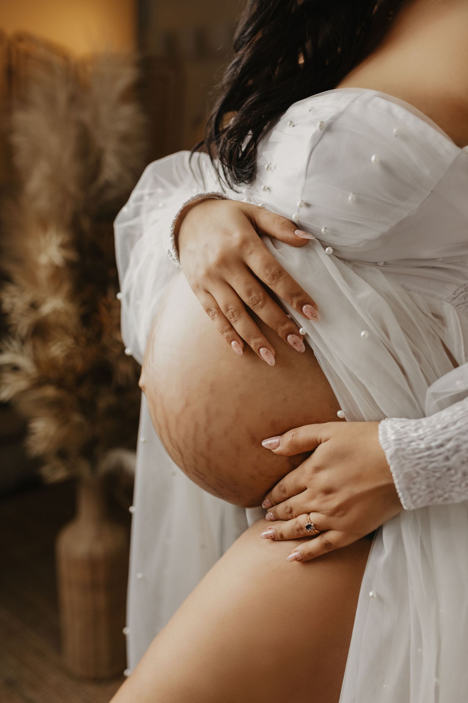 Close-up maternity photos showing pregnant belly in white lace dress.