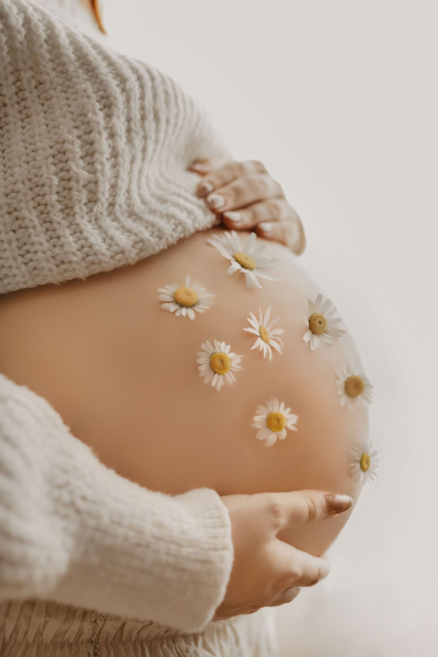 Artistic maternity photo showing pregnant belly adorned with delicate daisy flowers.