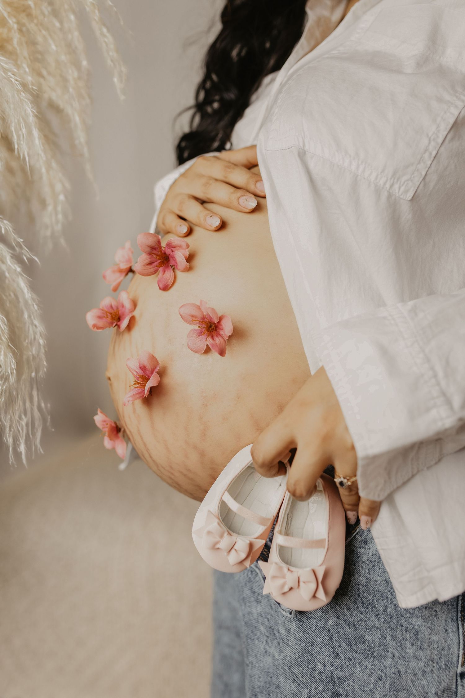 Artistic maternity photos with pink flowers placed on pregnant belly.