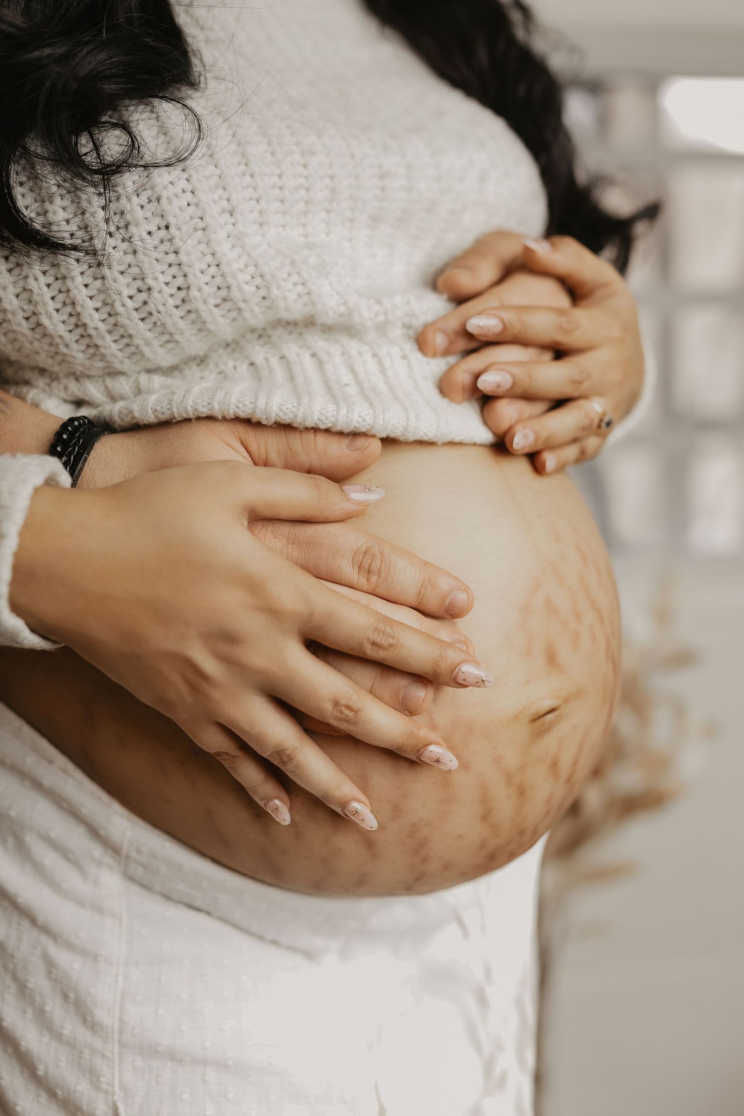Detail shots of hands cradling pregnant belly in white knit sweater.