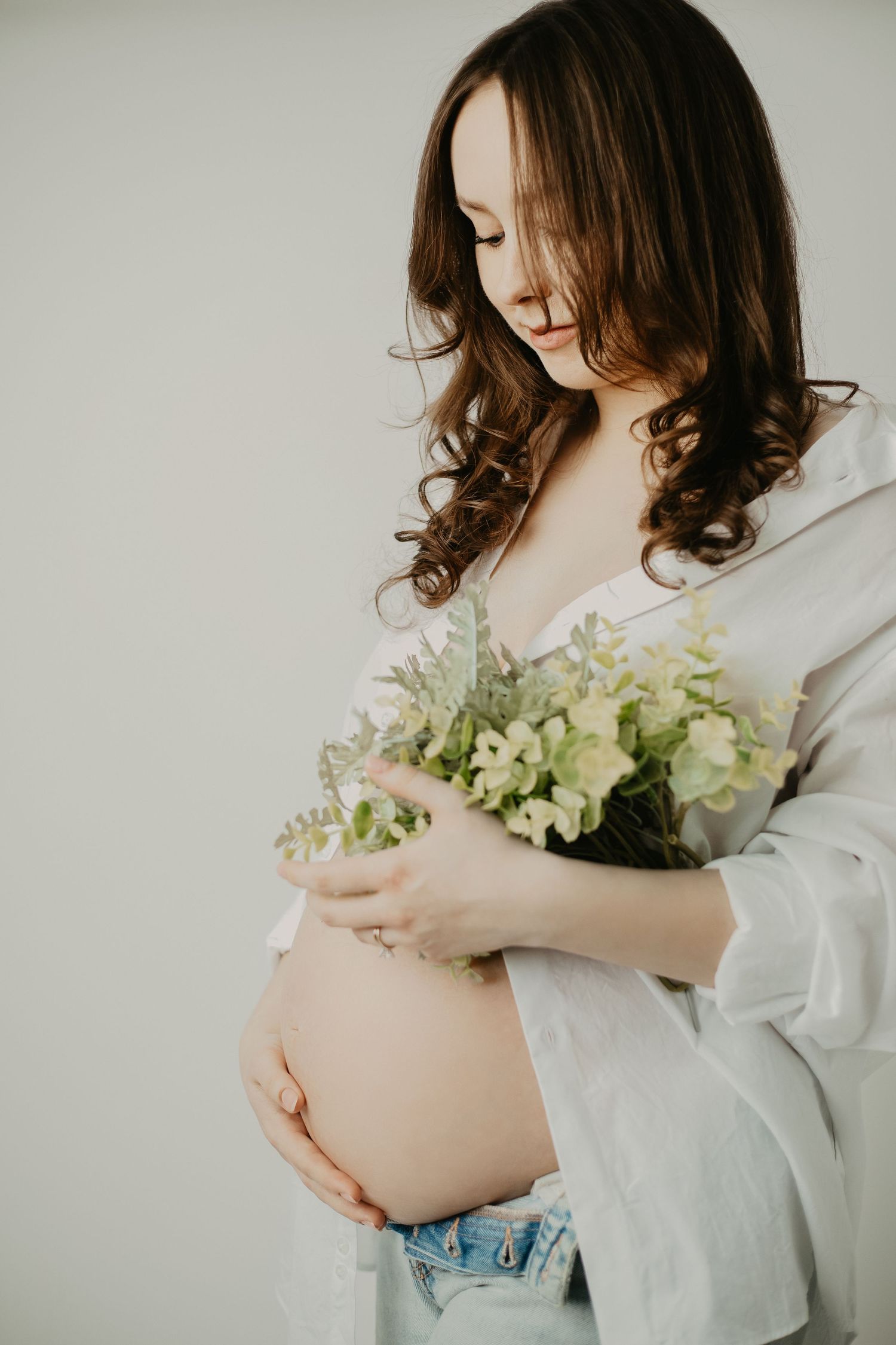 Maternity photo of an expectant mother in white shirt holding delicate white flowers against her baby bump.