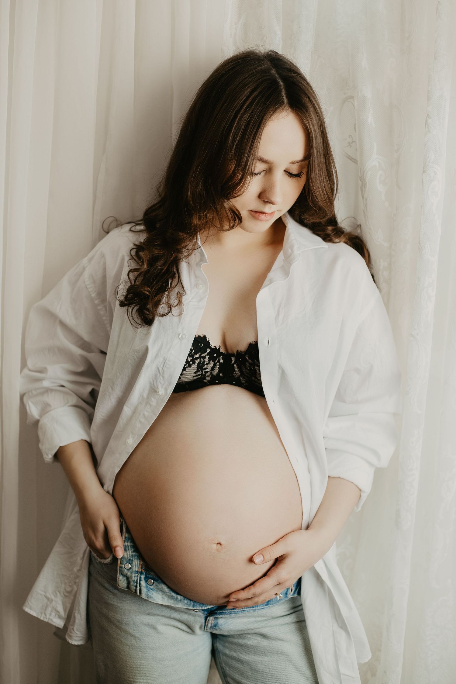 Artistic maternity photo featuring pregnant belly with white button-down shirt and denim.