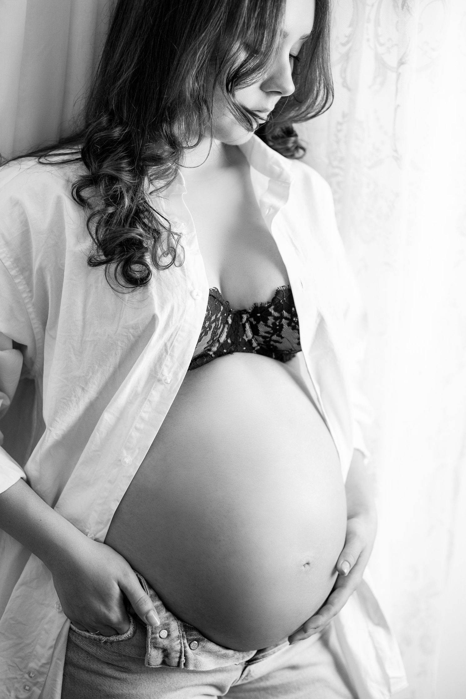 Black and white maternity portrait showing pregnant belly with white shirt and lace details.