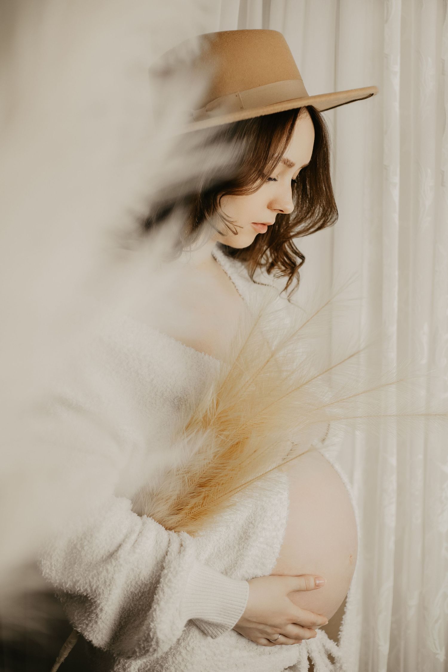 Dreamy maternity photo with tan hat and white sweater creating ethereal mood with soft lighting.