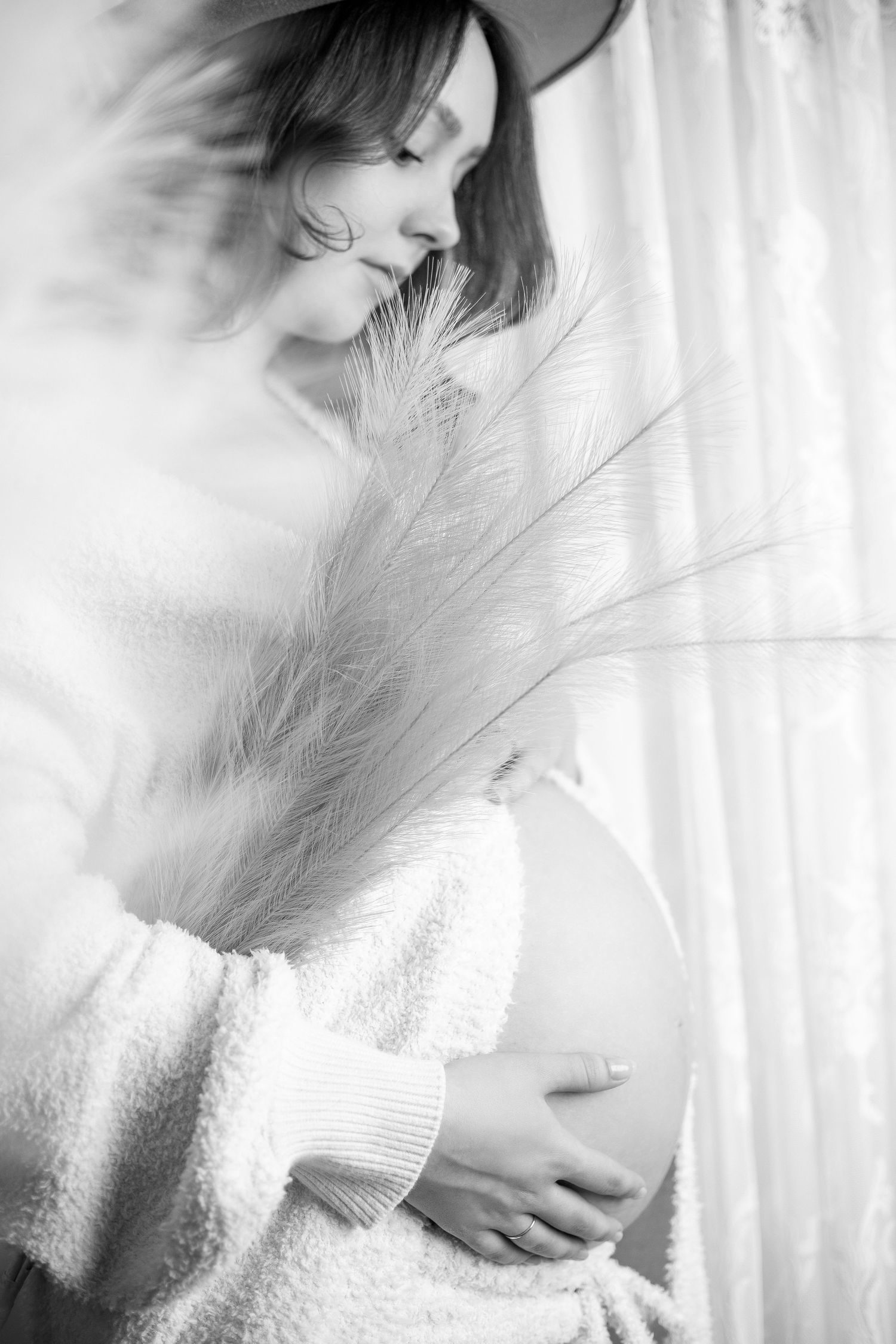 Ethereal black and white maternity photo with feather and soft sweater creating dreamy atmosphere.