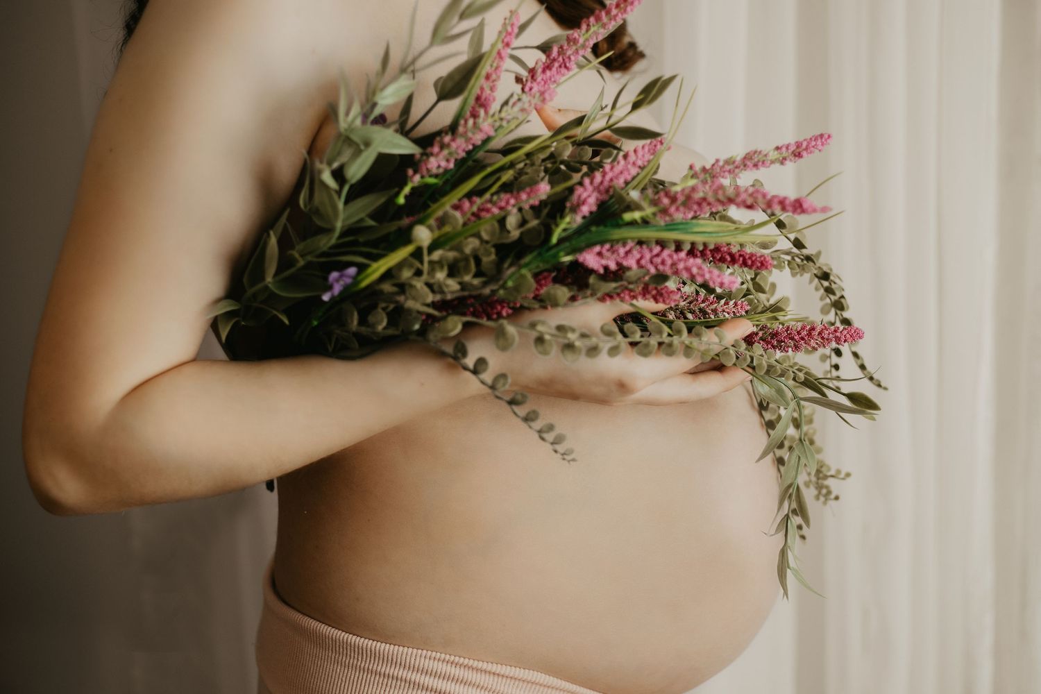 Artistic maternity photo showing pregnant belly with pink and green wildflowers.