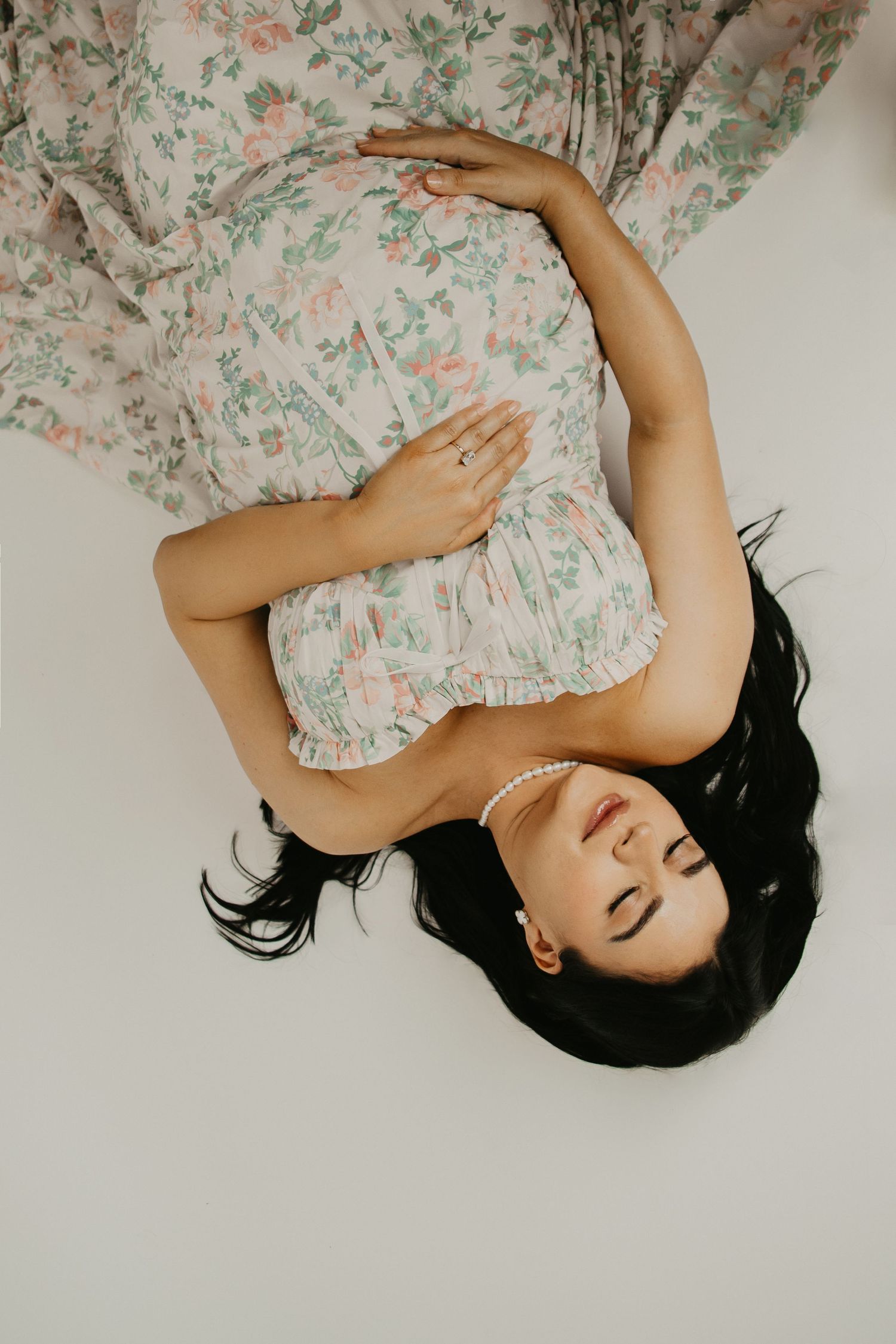 Artistic overhead portrait with flowing floral dress against white backdrop.