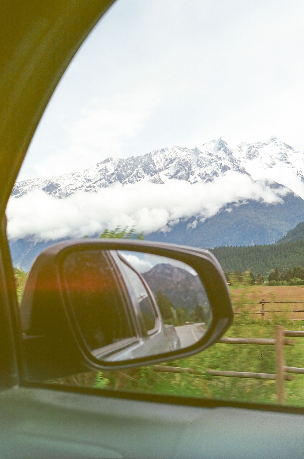 Snow-capped mountain peaks seen through car window with side mirror view.
