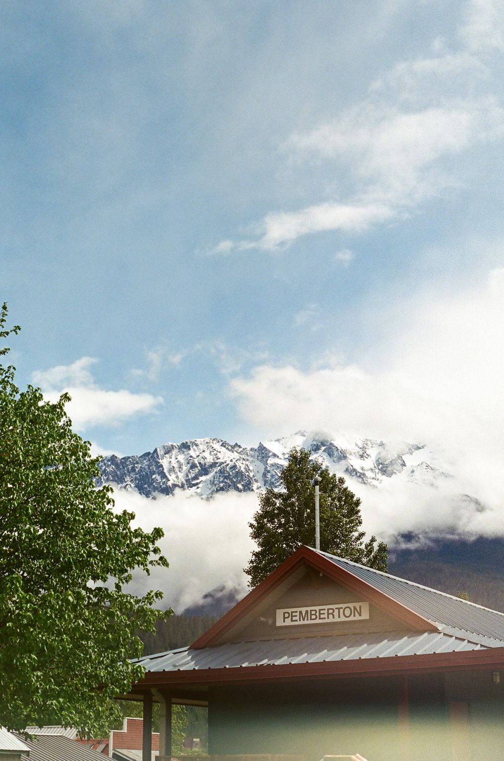 Mountain ridge with snow-covered peaks visible behind red-roofed building.
