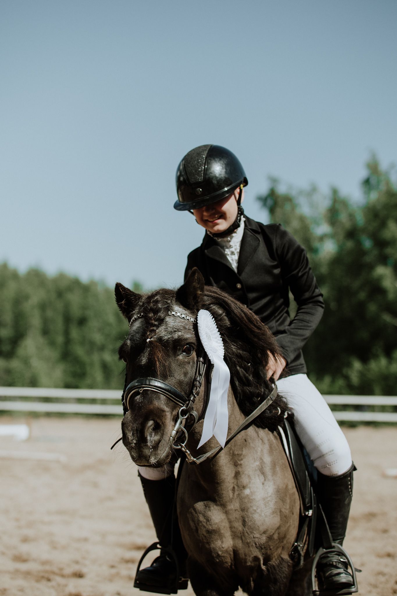 Competitive equestrian in formal attire riding a dark horse in an outdoor arena.