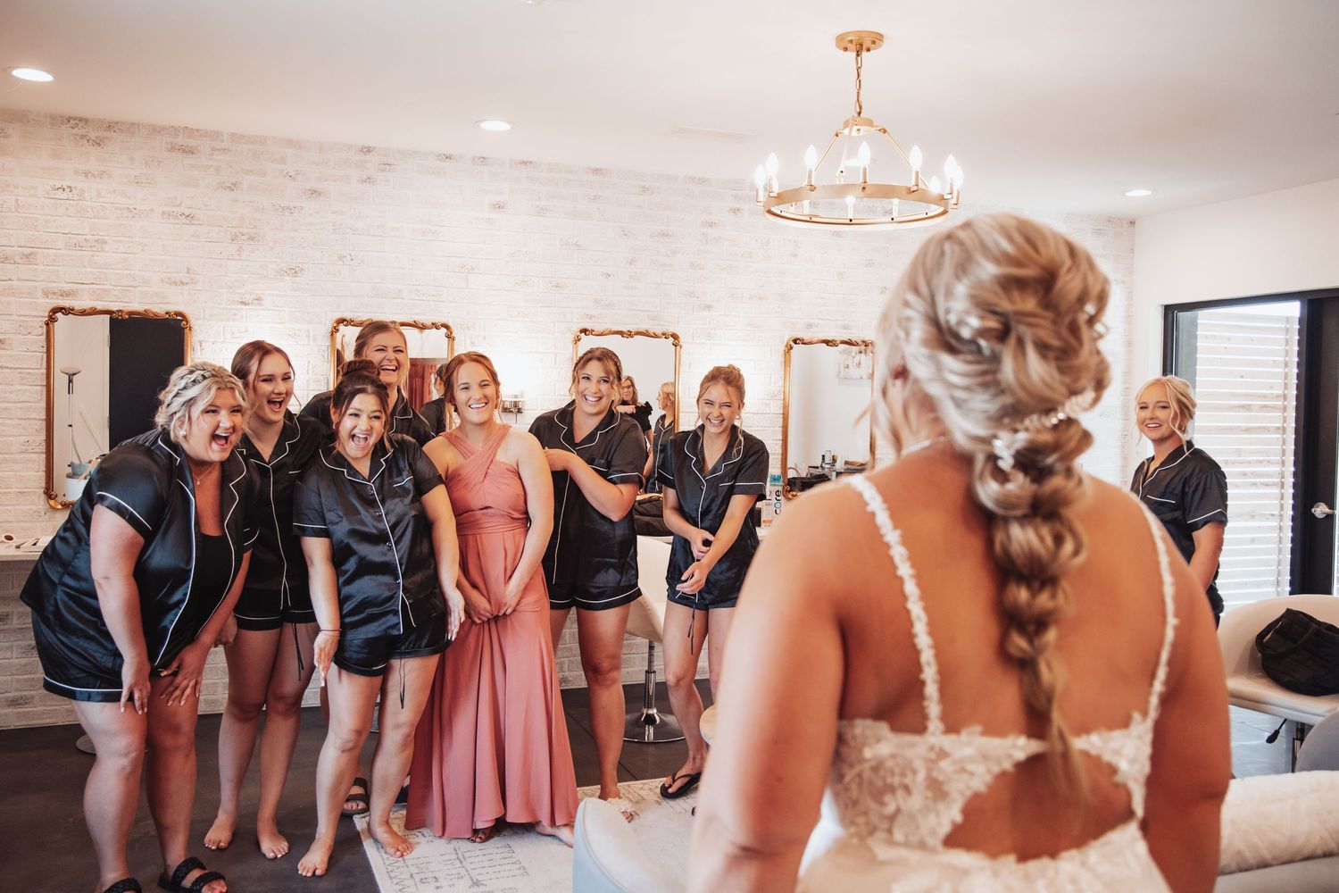 Wedding party gathering in elegant indoor venue with chandelier and white brick walls.