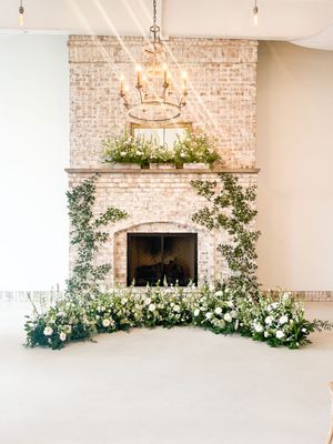 Ornate brick fireplace adorned with cascading white flowers and greenery beneath a vintage chandelier.