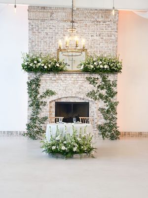 Elegant fireplace decorated with white flowers and greenery beneath a crystal chandelier.