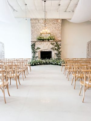 White ceremony space with wooden chairs and a beautifully decorated brick fireplace altar.