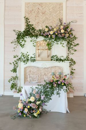 Elegant wedding photo backdrop with lush floral arrangements and greenery around a vintage white settee.