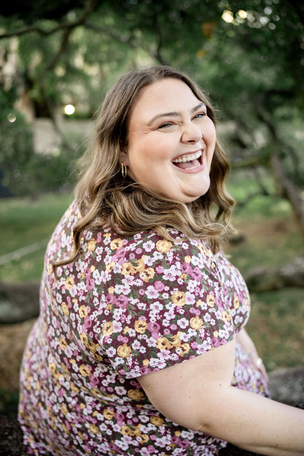 Woman in floral print dress laughing joyfully in natural outdoor setting.