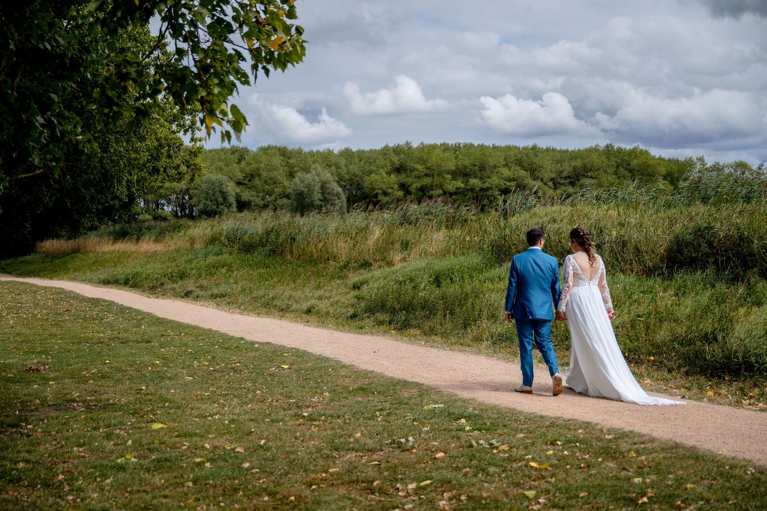 A couple walks along a winding dirt path through green coastal grasslands on a cloudy summer day.