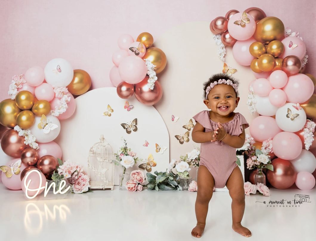 First birthday celebration setup with pink and gold balloon arch and decorative elements.