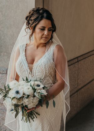 a beautiful bride with her hair in an updo and veil stands holding white bouquet looking over her shoulder during wedding portraits.
