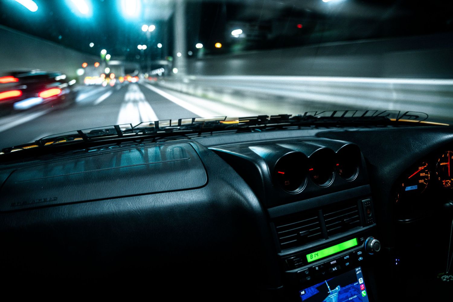Illuminated car dashboard at night shows glowing instrument panel with blue and green lights.