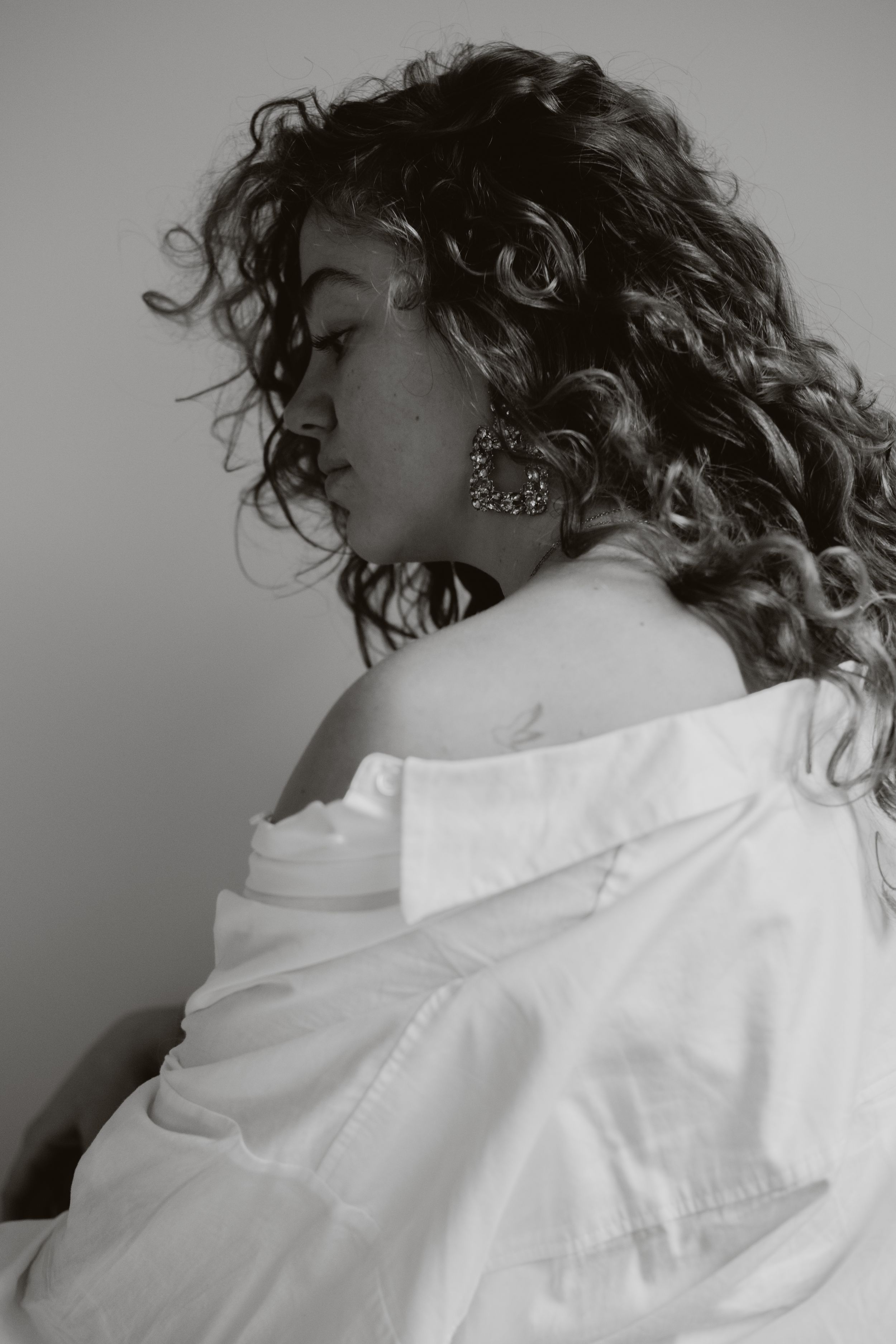Black and white profile portrait of a curly-haired woman in an off-shoulder white shirt.