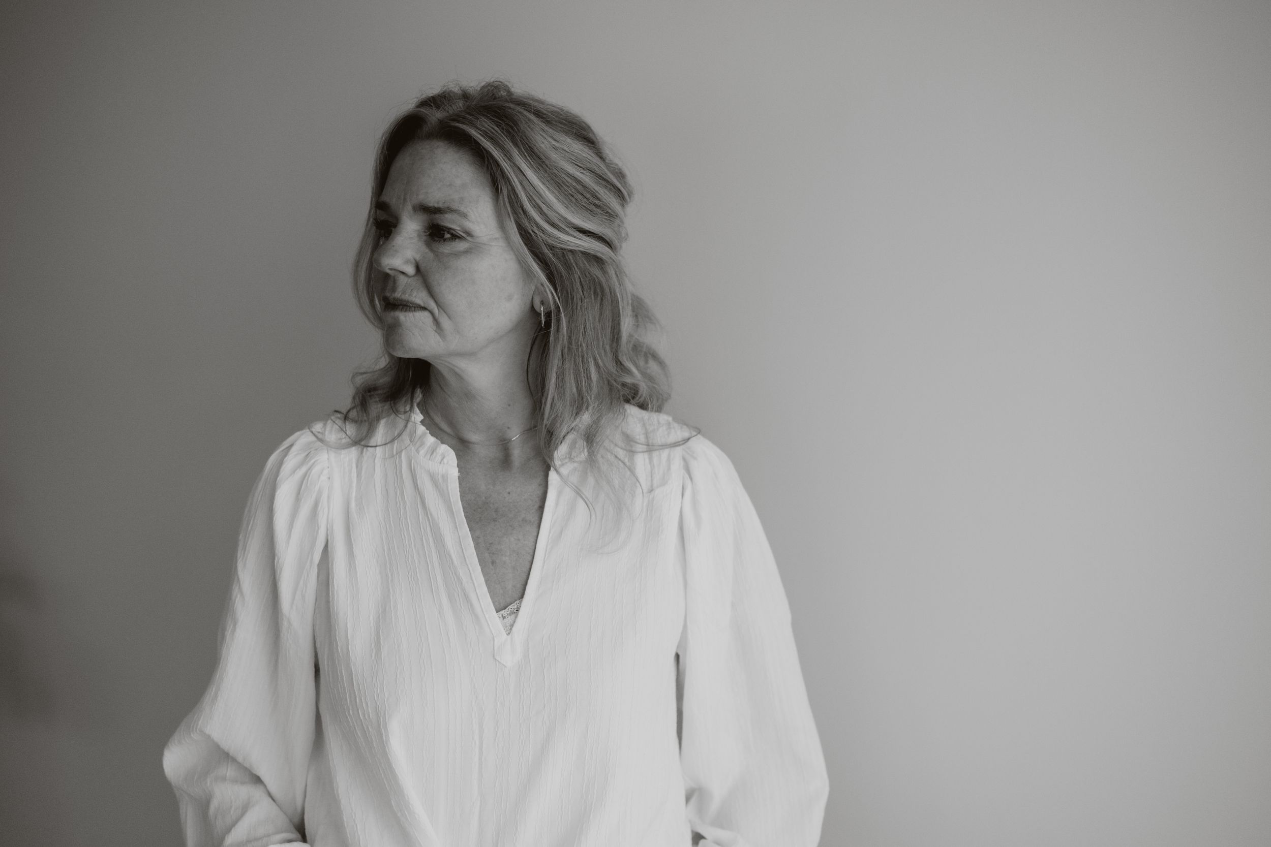 Black and white portrait of a blonde woman in a white blouse looking to the side thoughtfully.