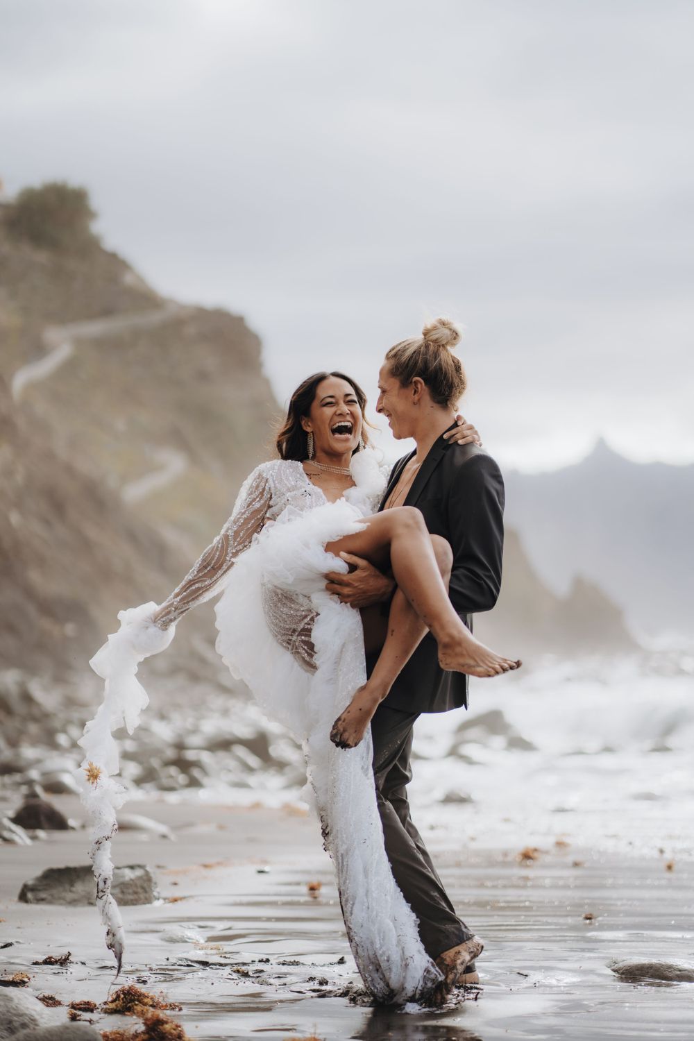 Joyful moment between couple during beach photoshoot with dramatic cliffs.