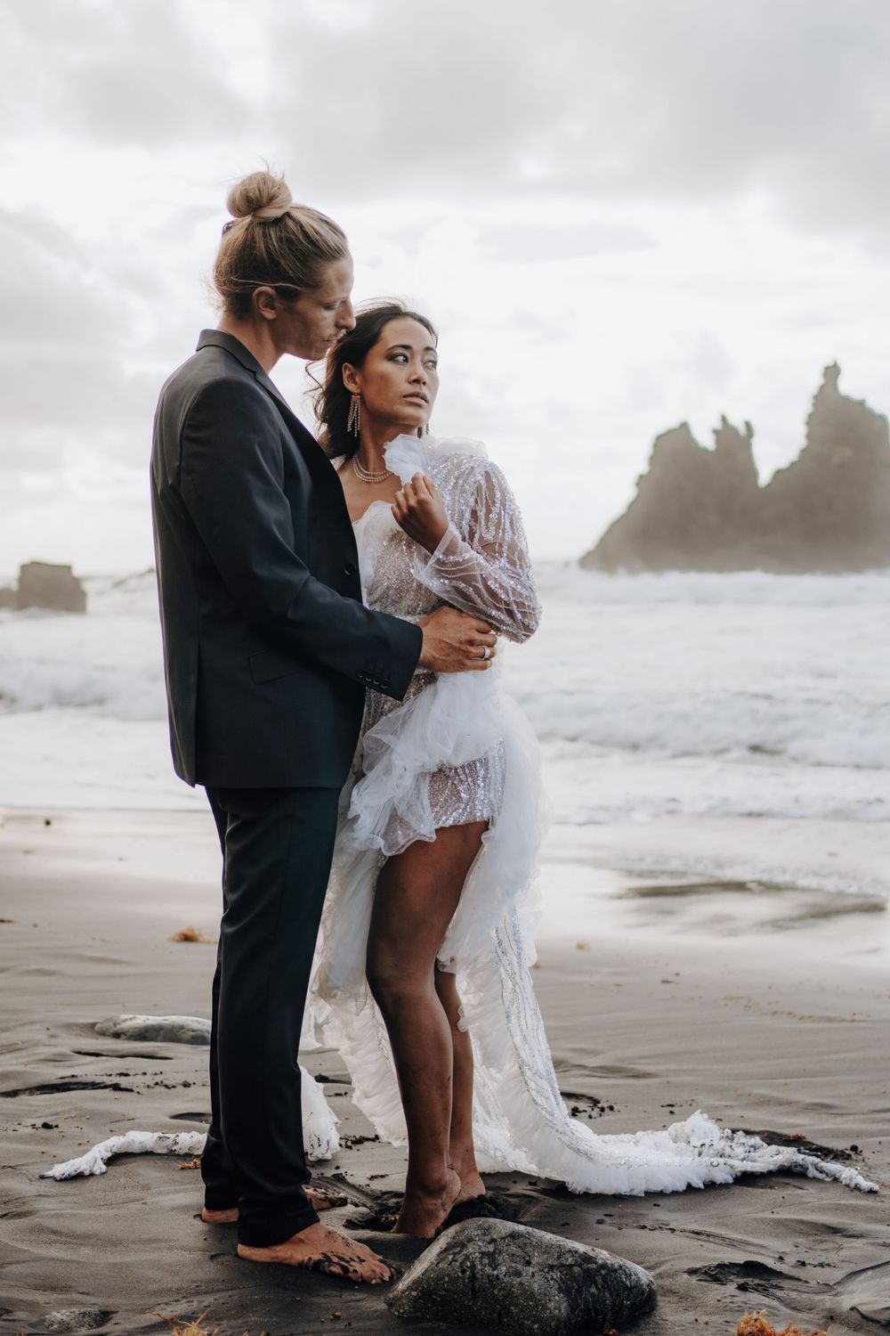 Intimate beach portrait with dark cliffs and moody ocean backdrop.