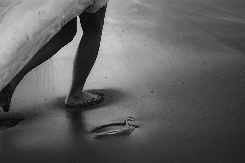 Close-up shot of bare feet walking on wet sand with rings lying nearby.