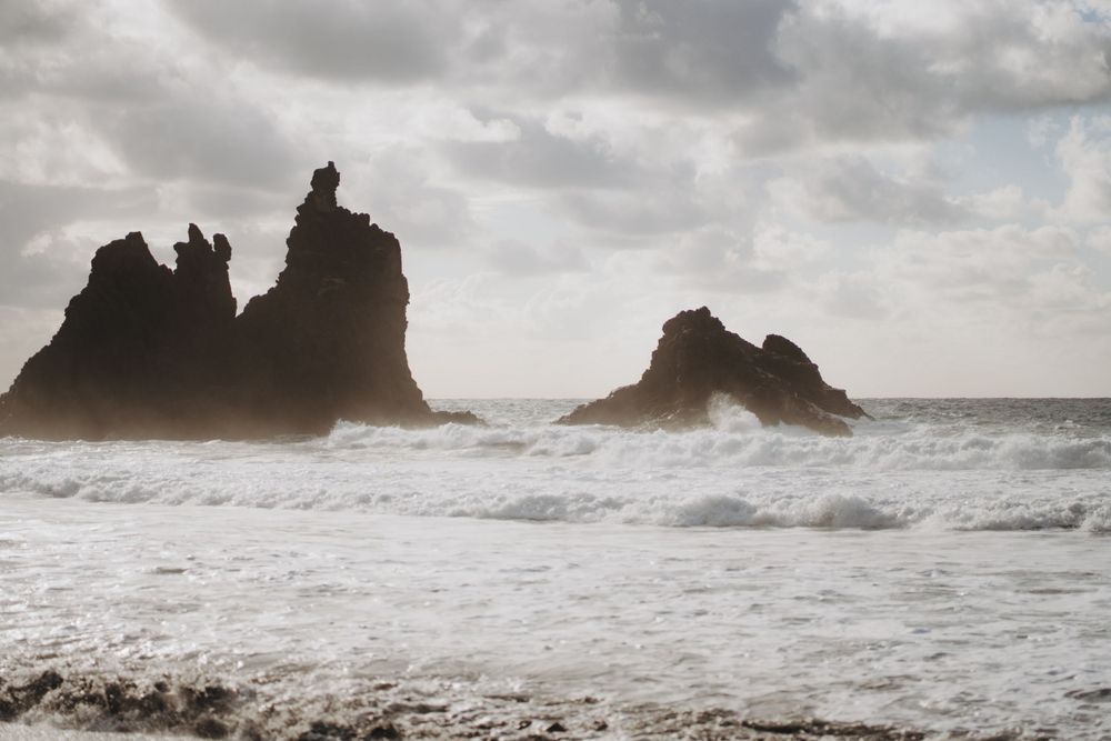 Dramatic rocky sea stacks rise from churning ocean waves under moody storm clouds.