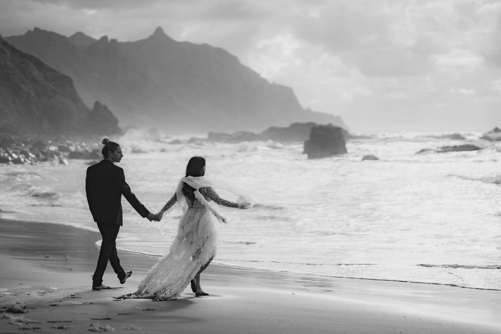 Two silhouettes walk hand in hand along a dramatic coastline with mountains in the background.