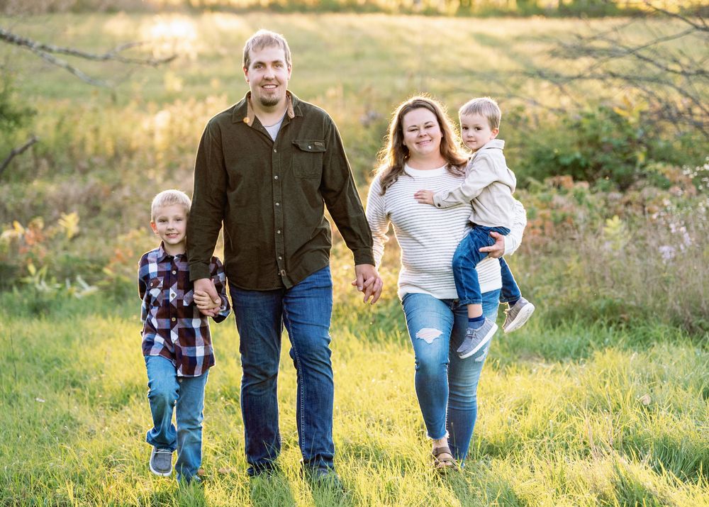 Family members walk together through a lush green meadow at sunset.