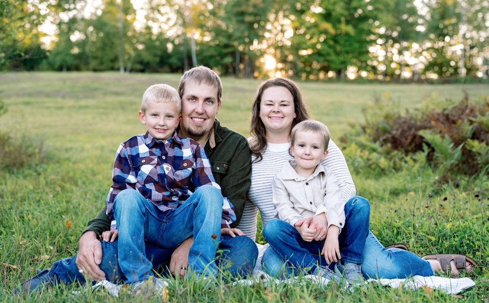 Family of four sitting together on blanket in grassy field during sunset.