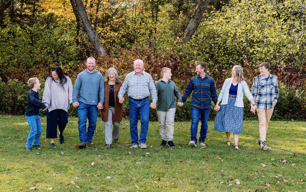 Large family holding hands walking together outdoors in autumn park with colorful fall foliage.