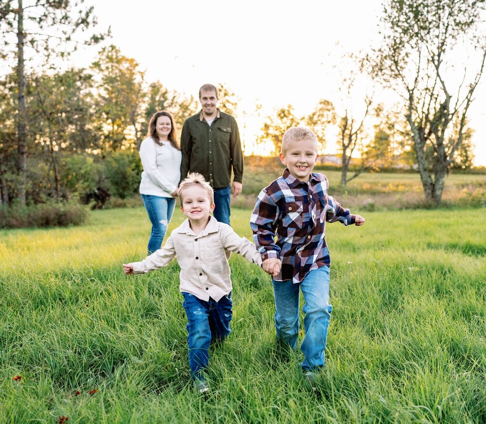 A family plays and runs together in a sunlit grassy field during golden hour.