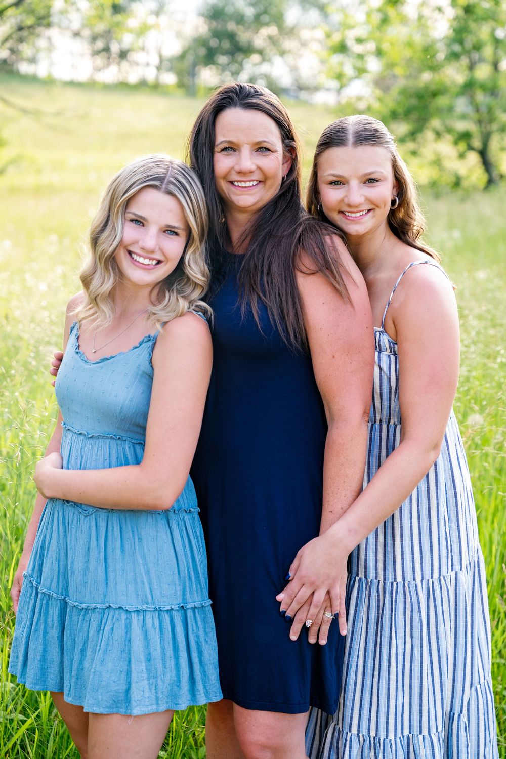 Four women in coordinating blue and navy dresses pose together in a sunny field.