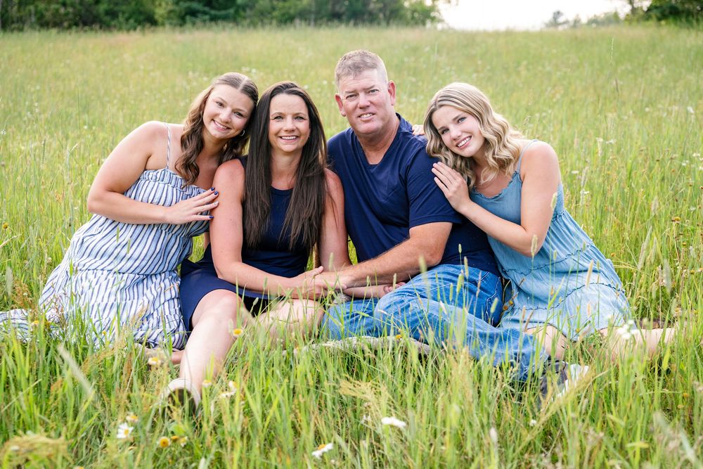A group relaxes together in tall grass during a summer photo session.