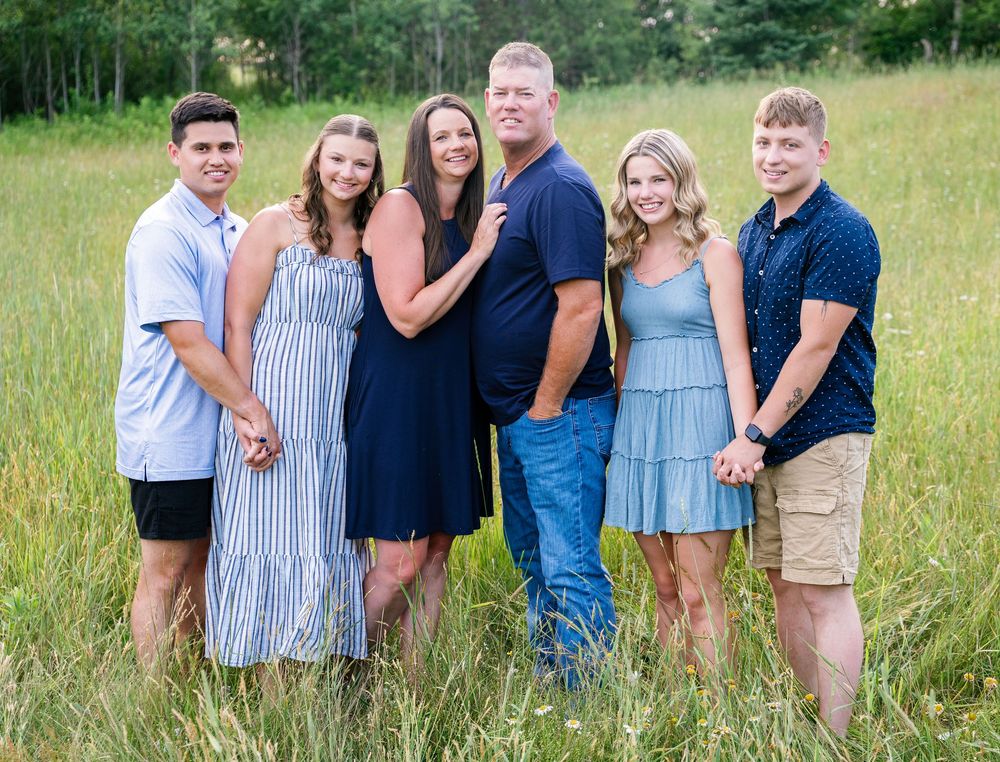 A family group poses together in casual attire against a natural outdoor backdrop.