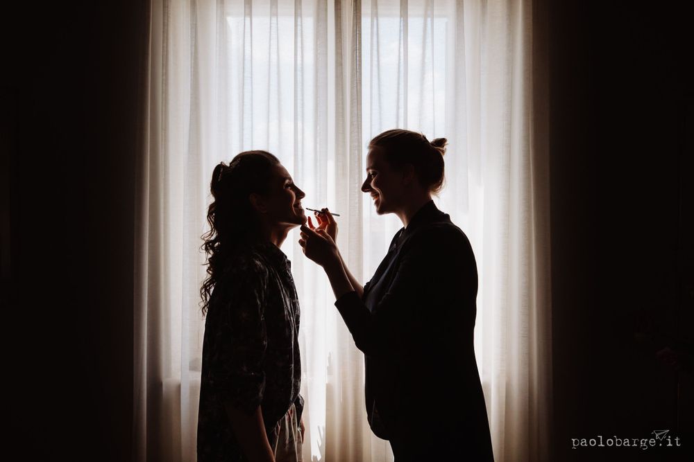 Silhouetted figures preparing for a wedding against a bright window backdrop.